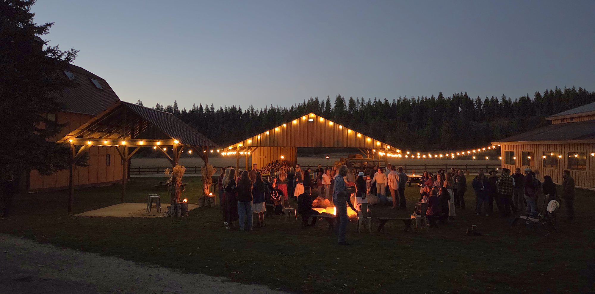 Guests gathered around the fire at dusk on October 3, with string lights on the wood shed and The Round Table